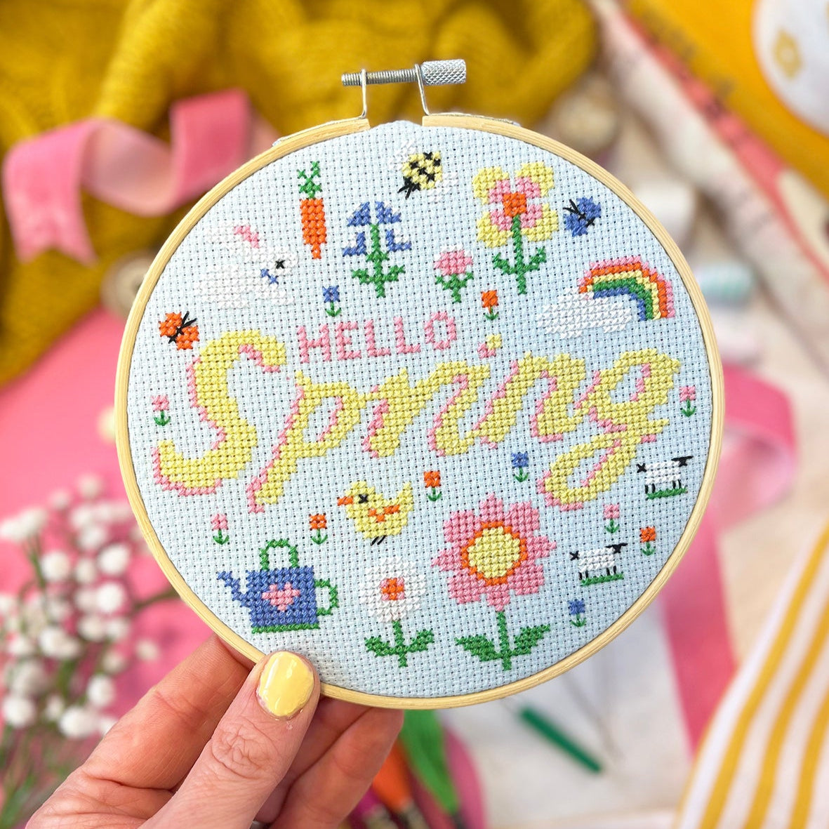 cross stitch design on blue aida with the wording 'hello spring'