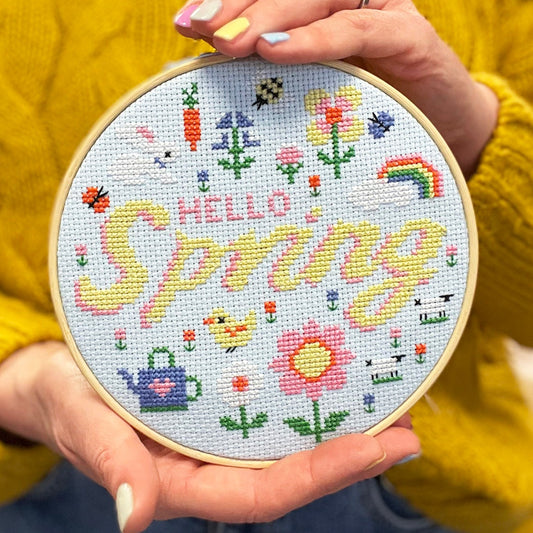 Cross stitch design with blue aida with the words 'hello spring' on it.