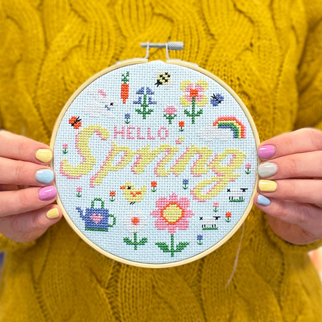 Cross stitch kit on blue aida with the words 'hello spring' on it.